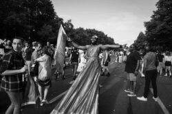 vogue Eine Person mit langem Gewand trägt eine Regenbogenfarbe die Arme weit ausgetreckt. CSD 2023.