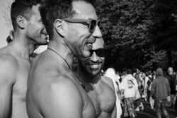 Anthony Drei Männer stehen links, die zwei Vorderen Oberkörperfrei und Sonnenbrillen. Breites Lachen. Eine Person schaut direkt in die Kamera. CSD 2023